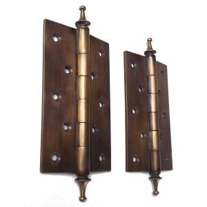 May include: Two antique brass hinges with decorative finials. The hinges are closed and have a distressed finish.