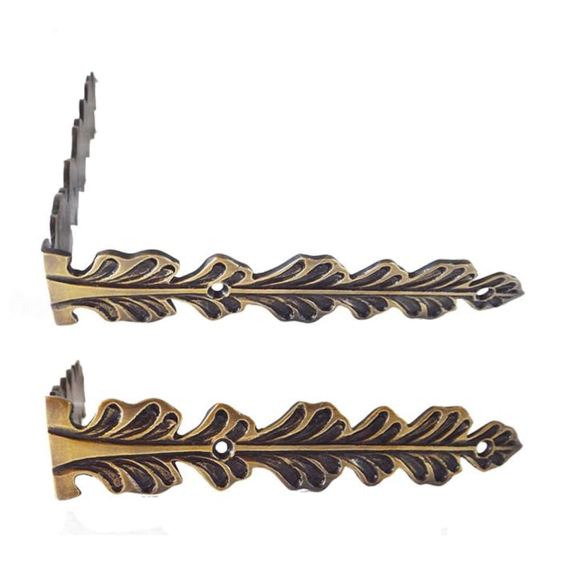 May include: Two antique gold corner brackets with a leaf design. The brackets are made of metal and have a decorative finish.