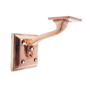 Könnte beinhalten: Eine kupferfarbene Metall-Regalhalterung mit quadratischer Basis und einem gebogenen Arm. Die Halterung ist für die Wandmontage konzipiert und kann zur Unterstützung eines Regals verwendet werden.