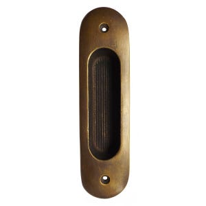 May include: A brass door pull with a rectangular cutout and rounded edges. The pull has a brushed finish and two small holes on either side of the cutout.