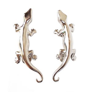 May include: A pair of silver gecko door handles. The geckos are facing each other with their tails curled around.