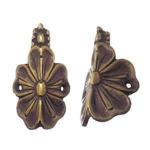 May include: Two antique bronze-colored flower-shaped cabinet pulls. Each pull features a detailed floral design with a central stud and two screw holes for mounting. The pulls have a weathered, aged appearance.