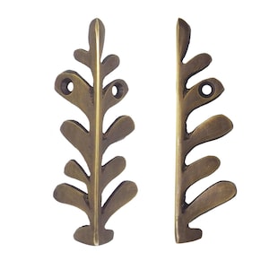 May include: Two bronze-colored leaf-shaped metal decorative elements. Each piece has a series of rounded, leaf-like shapes along a central stem. The top of each piece has two holes for mounting. The metal has a slightly aged appearance.