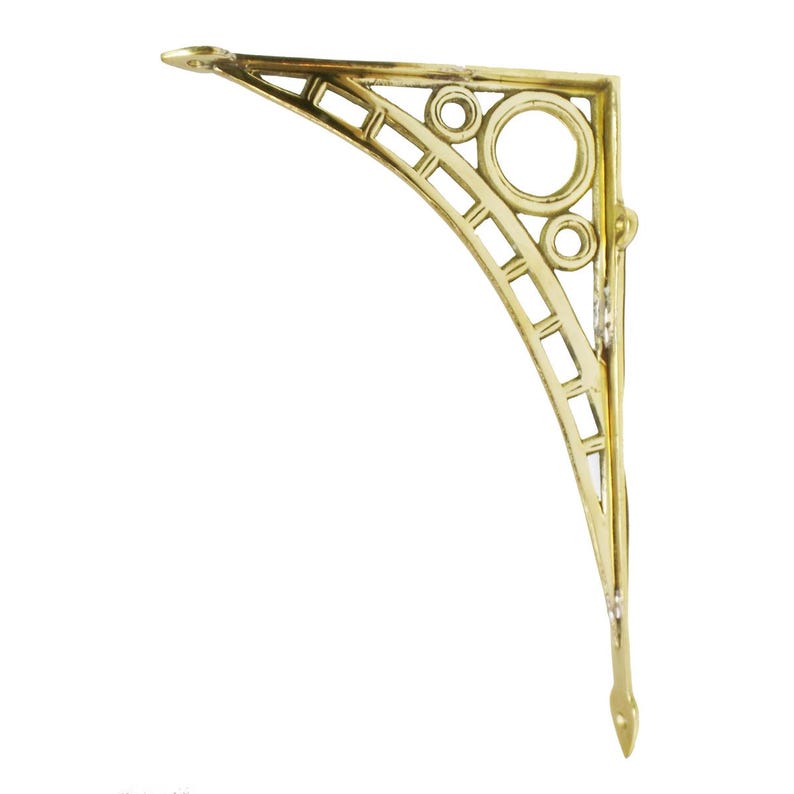 May include: A gold-colored, decorative shelf bracket with an ornate design. The bracket features a curved shape with geometric cutouts, circles, and a pointed end. It is designed to be mounted on a wall to support a shelf.