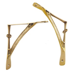 Puede incluir: Dos escuadras de estante de latón con un diseño curvo. Los soportes tienen un tono dorado cálido y presentan un diseño decorativo calado. Cada soporte tiene una parte superior plana para soportar un estante y orificios de montaje.