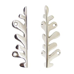 May include: Two silver-coloured leaf-shaped metal embellishments. Each piece has a series of rounded, leaf-like shapes along one side and three holes for attachment. The metal has a shiny, reflective surface.