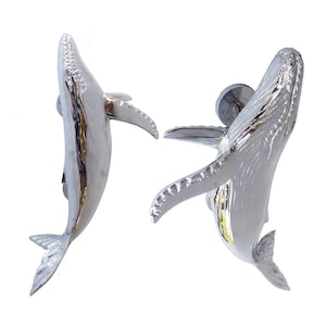 Puede incluir: Dos esculturas de ballenas plateadas en posición de salto. Las ballenas están detalladas con aletas y colas texturizadas.