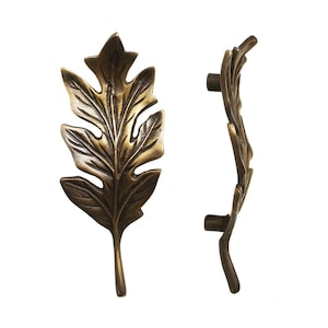 May include: A pair of antique brass leaf-shaped cabinet pulls. The pulls are detailed with a textured leaf design and have a curved shape.