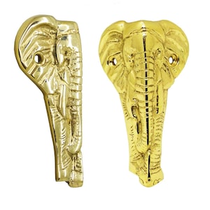 May include: Two brass elephant-shaped cabinet pulls. The pulls are gold-colored and feature detailed carvings of an elephant's head and trunk. Each pull has two holes for mounting. The elephant's head is facing forward on one pull and to the side on the other.