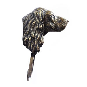 May include: A bronze sculpture of a dog's head with long, flowing ears. The sculpture is mounted on a metal stand.