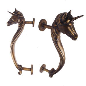 May include: Two bronze-colored unicorn door handles. Each handle features a unicorn head with a spiraled horn and a curved body. The handles are designed to be mounted on a door, with a round base and a connecting rod.