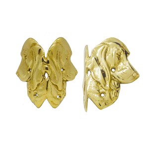 May include: Two brass-colored bookends, each shaped like a dog's head. One bookend features two dog heads facing each other, while the other depicts a single dog head in profile. The bookends have a glossy finish and are set against a white background.