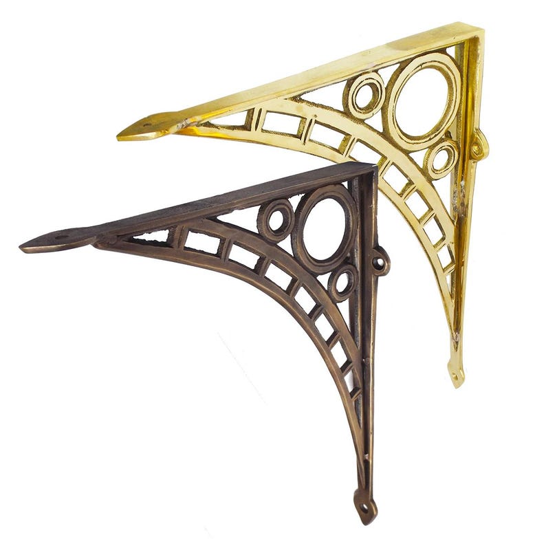 May include: Two decorative shelf brackets. One is gold-colored, the other is bronze. Both have an ornate design with circles and rectangular cutouts. The brackets are made of metal and are designed to support shelves.