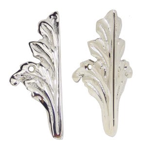 May include: Two silver-colored, leaf-shaped decorative furniture appliques. Each applique has a detailed, veined leaf design with a curved shape and a small hole for mounting. The appliques are made of a shiny, metallic material.