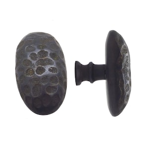 May include: Two dark bronze oval cabinet knobs with a hammered texture. One knob is shown from the front, and the other is shown from the side, revealing the stem. These decorative knobs are ideal for adding a rustic touch to furniture.