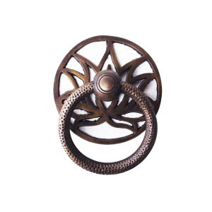 May include: Bronze-toned door knocker with a circular, floral-inspired backplate and a textured ring handle. The design features a central knob and intricate cut-out patterns, ideal for adding a touch of vintage charm to any door.