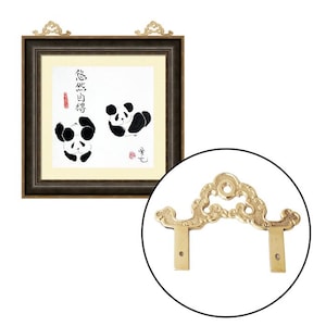 May include: A pair of gold-tone metal picture hangers with ornate designs. The hangers are attached to a dark brown picture frame with a white mat and a black and white illustration of two pandas. The illustration includes Chinese characters.