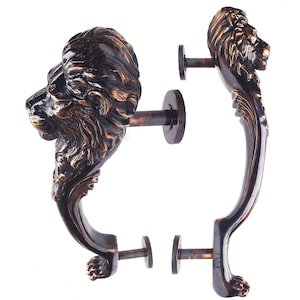 May include: Bronze-colored lion head door handles. The handles are detailed with a lion's mane and face, and have a curved handle design. The handles are mounted on a round plate with a rod for installation.