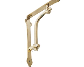 May include: A single, gold-colored shelf bracket with a decorative design. The bracket has a curved support and a flat top with pre-drilled holes for mounting. The metal has a polished finish, reflecting light.