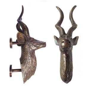 Puede incluir: Un par de manillas de puerta de bronce con forma de cabeza de antílope con cuernos largos y curvos. Las manillas están montadas en una pared con tornillos.