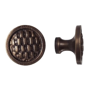 Op de afbeelding: Twee antieke bronzen kastknoppen. Eén is rond met een geweven textuur, de andere is een knop met een decoratief oppervlak en een korte steel. De knoppen zijn van metaal met een donkere, verouderde afwerking.