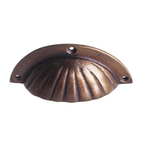 Op de afbeelding: Een bronzen schelpvormige trekker met een getextureerd oppervlak en drie voorgeboorde gaten voor montage. De trekker heeft een gebogen ontwerp en is geschikt voor kasten of meubels. De hardware is gemaakt van metaal.
