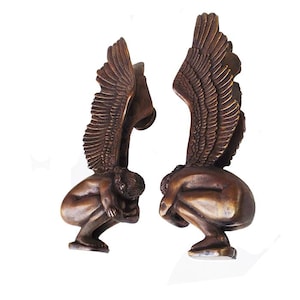 May include: A pair of bronze door handles in the shape of angels with wings. The angels are crouching with their heads bowed and their wings spread out behind them.