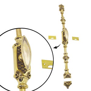 Könnte beinhalten: Ein detaillierter, goldfarbener Fensterriegel mit einem verzierten Design. Der Riegel hat einen dekorativen Griff mit einem Schachbrettmuster und einer ovalen Verzierung. Enthält zwei kleine, rechteckige Montageplatten.