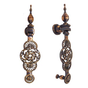 May include: Two ornate bronze door handles. Each handle features a decorative openwork design with floral and geometric patterns. The handles have a vintage aesthetic, with a dark bronze finish and intricate detailing.