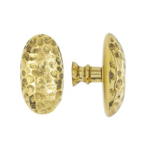 May include: Two brass oval door knobs with a hammered texture. One knob is positioned upright, while the other is on its side, showcasing the textured surface and the connecting stem.