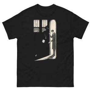 May include: A black short-sleeve t-shirt featuring a white graphic illustration of a person standing in an arched doorway. The scene depicts a dark, shadowy figure looming nearby, with a small window showing a cross symbol above the doorway.