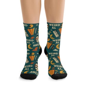 May include: A pair of teal socks with a repeating pattern of accordions, mustached faces, birds, moons, clouds, and the text "WEIRD AL". The socks have black heels and toes.