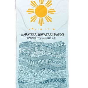May include: A white beach towel with a gradient blue background. The top features a yellow sun graphic and the text "WAKATERAHKWATARIHÀ:TON, WARMING MYSELF IN THE SUN". The bottom has a blue and white patterned design.