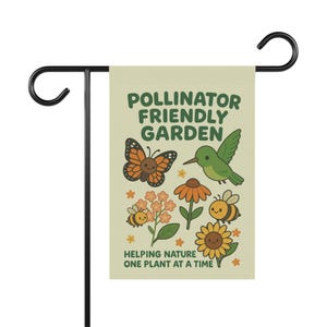 Puede incluir: Una bandera de jardín crema con el texto "Pollinator Friendly Garden" e ilustraciones de una mariposa, un colibrí, abejas y flores. La bandera está sobre un soporte de metal negro.