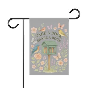 May include: A gray garden flag featuring a whimsical design with a small green book house, birds, butterflies, and flowers. The flag has the text "Take a Book, Share a Book" in a decorative font. The flag is attached to a black metal garden stake.