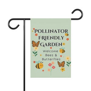 Könnte beinhalten: Eine Gartenflagge auf einem schwarzen Metallständer. Die hellgrüne Flagge zeigt den Text "Pollinator Friendly Garden" mit Illustrationen von Bienen, Schmetterlingen und Blumen. Auf der Flagge steht auch "Welcome Bees & Butterflies."