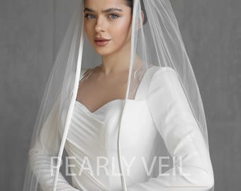 May include: A white bridal veil with a satin trim. The veil is worn by a woman with dark hair and a white dress. The text "PEARLY VEIL" is visible on the dress.