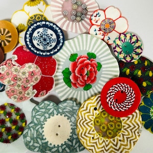 Może przedstawiać: Kolekcja dekoracyjnych podkładek w różnych kształtach i wzorach. Podkładki mają wzory kwiatowe, geometryczne kształty i żywe kolory, w tym czerwony, żółty, niebieski i zielony. Niektóre mają kształt kwiatu, inne są okrągłe lub w kształcie płatka.