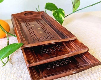 Può includere: Tre vassoi da portata in legno con intagli intricati e una finitura marrone scuro. Il vassoio superiore presenta un motivo decorativo e accenti dorati.
