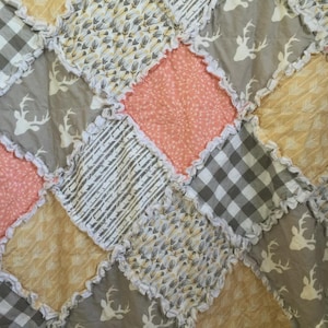 Puede incluir: Un edredón de patchwork con una variedad de telas en tonos grises, melocotón y amarillo. El edredón tiene un borde con volantes e incluye patrones como cuadros, siluetas de ciervos y diseños florales. La estética general es rústica y acogedora.