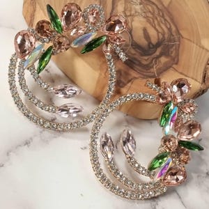 May include: A pair of gold hoop earrings with a double row of clear rhinestones. The hoops are adorned with pink and green crystal accents.