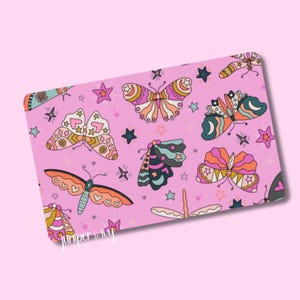 May include: A rectangular pink surface with a repeating pattern of colorful butterflies and stars. The butterflies feature various designs and colors, including orange, pink, and teal. The text "Juniper & Ivy" is in the lower left corner.