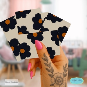 May include: Playing cards with a floral design. The cards feature a cream background with navy blue flowers and orange centers. The text "Standard card size" is visible. The Juniper & Ivy logo is in the bottom right corner.