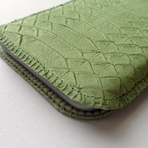 Könnte beinhalten: Eine grüne Leder Handyhülle mit einem genähten Rand und einem dezenten Prägemuster.