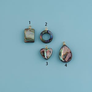 May include: Four iridescent abalone shell pendants in various shapes: a rectangle, a circle, a heart, and a teardrop. Each pendant has a gold-colored bail for attaching to a chain or cord. The pendants are displayed on a light blue background.