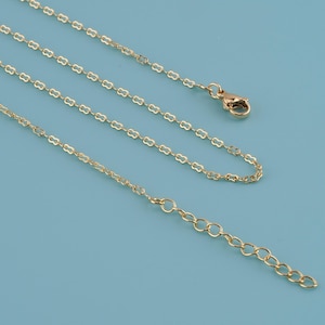 May include: A delicate gold-colored necklace with a clover-shaped chain design. The necklace features a lobster clasp closure and an adjustable chain. The jewelry is displayed on a light blue background.