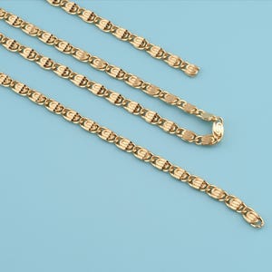 May include: Gold-colored chain necklace with a repeating oval and curved design. The necklace is displayed on a light blue background. The chain is made of a shiny metal.