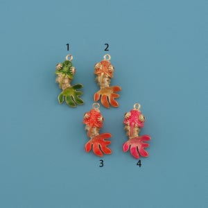 Può includere: Quattro ciondoli colorati a forma di pesce rosso con dettagli color oro. I ciondoli sono in tonalità di verde, arancione, rosso e rosa. Ogni ciondolo ha un anello nella parte superiore per il fissaggio a gioielli o altri oggetti artigianali. Lo sfondo è azzurro chiaro.