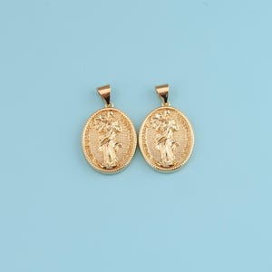 Peut inclure: Deux pendentifs ovales dorés avec un motif en relief détaillé. Chaque pendentif représente une figure tenant un arrangement floral, dans un cadre texturé. Les pendentifs ont une boucle en haut pour une chaîne, sur fond bleu clair.