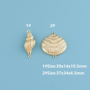 May include: Two gold-colored seashell charms. One is a spiral conch shell, and the other is a fan-shaped scallop shell. The conch shell measures 1.5 x 0.5 x 0.4 inches. The scallop shell measures 1.4 x 1.3 x 0.3 inches. Text indicates sizes.